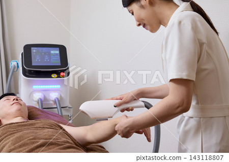 Close-up of a man receiving arm hair removal treatment from a beauty staff member. Close-up of a man receiving arm hair removal treatment from a beauty staff member. 143118807