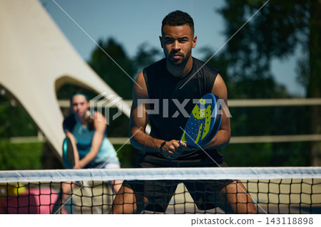 Focused male padel player in ready stance near net during professional doubles game Focused male padel player in ready stance near net during professional doubles game 143118898