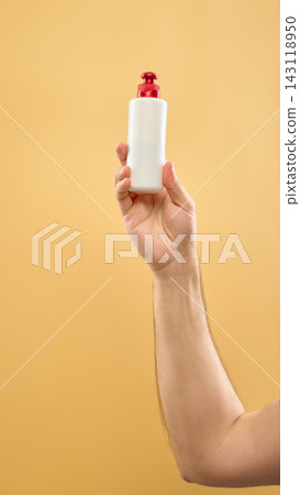 Hand holding white skincare bottle with red pump on soft yellow background. Hand holding white skincare bottle with red pump on soft yellow background. 143118950