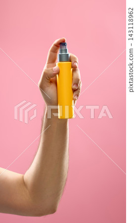 Hand holding bright cosmetic spray bottle on pink studio background Hand holding bright cosmetic spray bottle on pink studio background 143118962