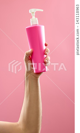 Hand holding pink pump bottle with skincare product on pastel background 143118963