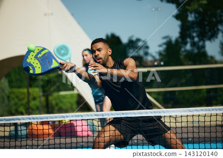 Professional male padel player lunging toward fast ball at net during competitive rally Professional male padel player lunging toward fast ball at net during competitive rally 143120140