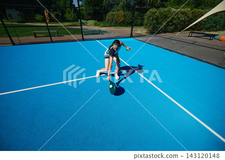 Male padel athlete in black sportswear moving dynamically across minimalist blue outdoor court Male padel athlete in black sportswear moving dynamically across minimalist blue outdoor court 143120148