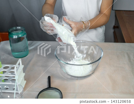 Person mixing white powder into a glass bowl while wearing gloves for a home science experiment Person mixing white powder into a glass bowl while wearing gloves for a home science experiment 143120658