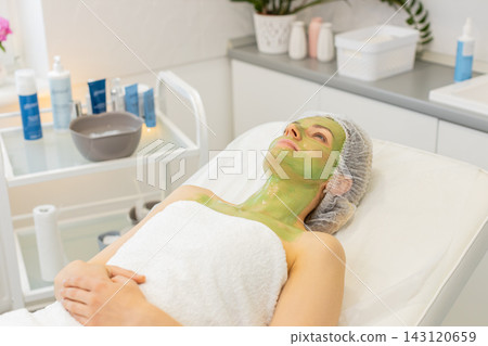 Caucasian woman lying with dried green peeling mask on face and neck during beauty clinic spa care Caucasian woman lying with dried green peeling mask on face and neck during beauty clinic spa care 143120659