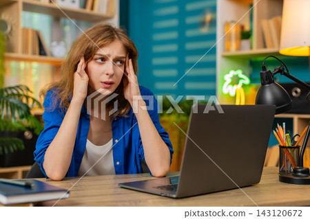 Young woman on home table rubbing temples feeling tired after long laptop work in cozy living room Young woman on home table rubbing temples feeling tired after long laptop work in cozy living room 143120672