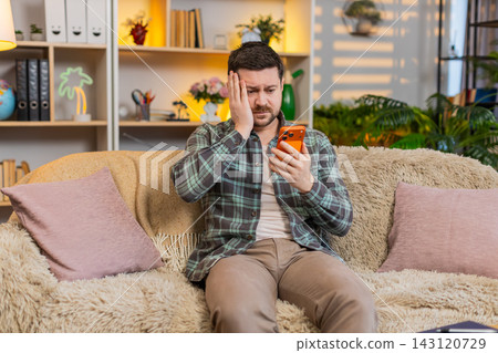 Young man on home sofa upset after bad lottery result on smartphone feeling loss and disappointment Young man on home sofa upset after bad lottery result on smartphone feeling loss and disappointment 143120729