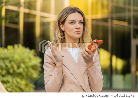 Young woman discussing work on speakerphone walking in city street with focused business expression Young woman discussing work on speakerphone walking in city street with focused business expression 143121172