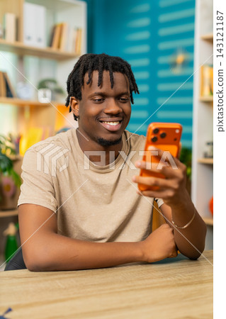 African American young man on home table reading smartphone message and smiling with good news joy 143121187