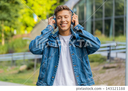 Young man listening to music on headphones walking in city street with happy relaxed smile outdoors 143121188