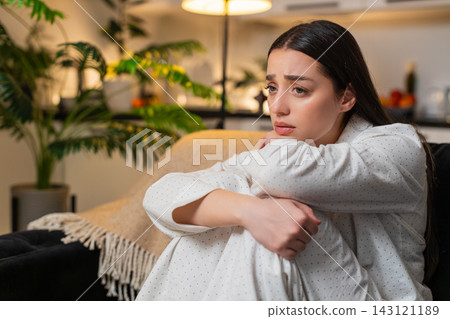Young woman sits curled up hugs knees stressed by bad news depressed silent mood evening sigh alone 143121189