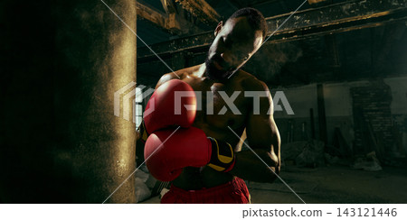 Professional boxer lowers his gloves beside a heavy bag with exhausted resilience Professional boxer lowers his gloves beside a heavy bag with exhausted resilience 143121446