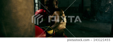 Powerful boxer strikes a heavy bag in a dark industrial gym with fierce determination Powerful boxer strikes a heavy bag in a dark industrial gym with fierce determination 143121455