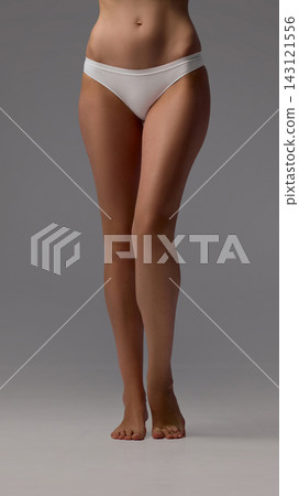 Cropped female hips and smooth legs in white panties on gray studio background Cropped female hips and smooth legs in white panties on gray studio background 143121556