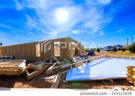 Construction activity is ongoing at site with wood Construction site with building materials roofing joins framing framing materials Construction activity is ongoing at site with wood Construction site with building materials roofing joins framing framing materials 143121656