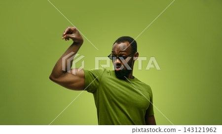Stylish man in sunglasses flexes muscular arm in green studio with proud confidence 143121962
