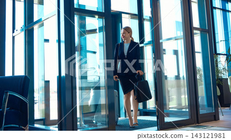 Female executive enters airport lobby carrying a laptop bag with cheerful anticipation 143121981