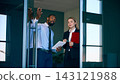 Male manager gestures while discussing travel plans with female colleague near airport entrance with confident focus Male manager gestures while discussing travel plans with female colleague near airport entrance with confident focus 143121988