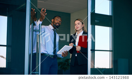 Male manager gestures while discussing travel plans with female colleague near airport entrance with confident focus Male manager gestures while discussing travel plans with female colleague near airport entrance with confident focus 143121988