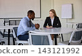 Businesswoman interviews a male professional at a table in airport meeting room with focused attention Businesswoman interviews a male professional at a table in airport meeting room with focused attention 143121992