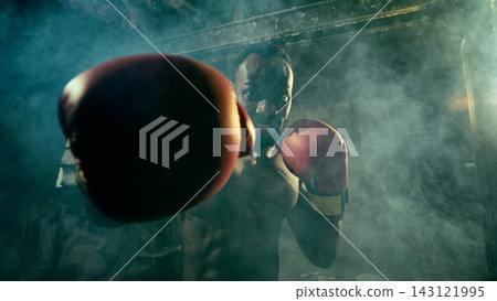 Intense boxer punches directly toward the viewer in a smoky industrial gym Intense boxer punches directly toward the viewer in a smoky industrial gym 143121995