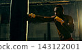 Skilled boxer lands a straight punch on a heavy bag with precise control Skilled boxer lands a straight punch on a heavy bag with precise control 143122001
