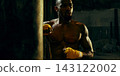Sweaty athlete pauses beside a punching bag with determined exhaustion Sweaty athlete pauses beside a punching bag with determined exhaustion 143122002