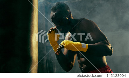 Concentrated combat athlete raises wrapped fists in a smoky gym with disciplined focus Concentrated combat athlete raises wrapped fists in a smoky gym with disciplined focus 143122004