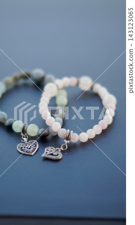 Two pale green and pink beaded necklaces with silver heart pendants are arranged together on a dark blue surface. The harmonious pair represents companionship, tenderness, and emotional bonds Two pale green and pink beaded necklaces with silver heart pendants are arranged together on a dark blue surface. The harmonious pair represents companionship, tenderness, and emotional bonds 143123065