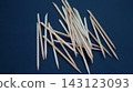 Pointed wooden manicure sticks are loosely scattered in overlapping directions on a dark blue background. The dynamic arrangement represents disorder, spontaneity, and the practical routine of 143123093