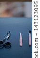 Black scissors, a slim pink grooming tool, and a small brush are arranged on a dark tabletop. Minimal grooming accessories symbolize personal care, precision, and everyday beauty routine. 143123095