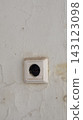 A small square electrical socket or wall fitting with a dark circular opening is mounted on a cracked and weathered plaster wall. The image represents aging infrastructure, utility, and small traces 143123098