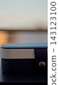 The corner of a blue storage case with white trim and a metal latch appears in a narrow vertical frame. The selective composition represents protection, organization, portability, and careful storage 143123100