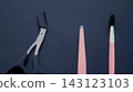 Black cuticle nippers, a pink nail file, and a manicure brush are arranged on a dark blue surface. Professional grooming tools represent precision, hygiene, and an organized personal care routine. 143123103