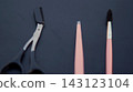 Black cuticle nippers, a pink nail file, and a manicure brush are aligned on a dark blue surface. Neatly spaced grooming tools represent precision, hygiene, order, and professional nail care. 143123104