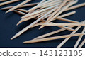 Pointed wooden manicure sticks fill the frame in a close-up view on a dark blue background. The dense pattern emphasizes texture, repetition, precision, and the routine of professional nail care. 143123105