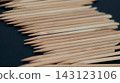 A large pile of pointed wooden manicure sticks is arranged diagonally on a dark background. Repetitive disposable beauty tools symbolize hygiene, precision, order, and professional nail care. 143123106