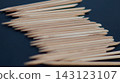 Pointed wooden manicure sticks form a dense diagonal pile on a dark blue background. Repetitive disposable nail tools represent order, hygiene, precision, and professional beauty care. 143123107