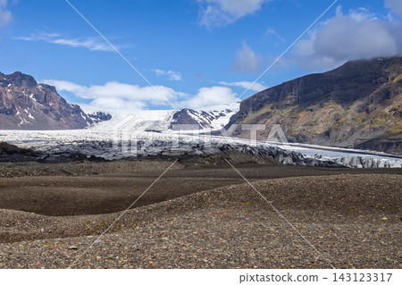 Wide landscape view of debris-streaked glacier tongue beyond rocky forefield in Iceland Wide landscape view of debris-streaked glacier tongue beyond rocky forefield in Iceland 143123317