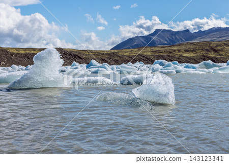 Floating icebergs in Fjallsarlon glacial lagoon with mountains, Iceland Floating icebergs in Fjallsarlon glacial lagoon with mountains, Iceland 143123341