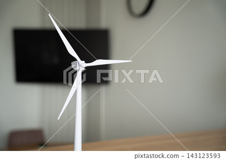 White wind turbine model standing on a table in a modern indoor setting. Clean energy renewable power and sustainable technology education White wind turbine model standing on a table in a modern indoor setting. Clean energy renewable power and sustainable technology education 143123593