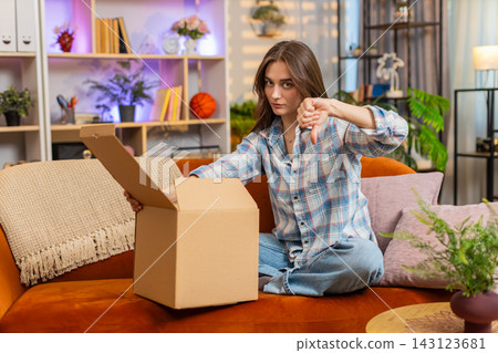 Young woman on home sofa unpacking delivery box feeling upset about order mistake and shopping error Young woman on home sofa unpacking delivery box feeling upset about order mistake and shopping error 143123681
