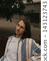 Guy with long hair sitting on a bench in a city park during the afternoon 143123743