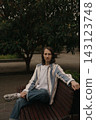 Guy with long hair sitting on a bench in a park during daytime 143123748