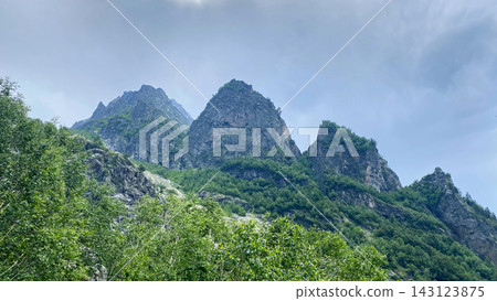 Clouds gather above rocky peaks, low angle view along the Shdugra Waterfall trail near Mazeri in Svaneti, Georgia Clouds gather above rocky peaks, low angle view along the Shdugra Waterfall trail near Mazeri in Svaneti, Georgia 143123875