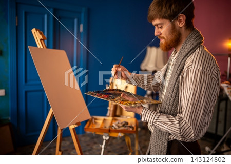 An artist painting on canvas in cozy studio with warm light An artist painting on canvas in cozy studio with warm light 143124802