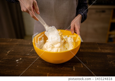 Hands mixing thick dough in bright yellow bowl on rustic wooden table under warm kitchen light Hands mixing thick dough in bright yellow bowl on rustic wooden table under warm kitchen light 143124818