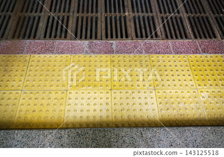 Top view of yellow tactile paving tiles with drainage grid providing barrier free environment for visually impaired 143125518