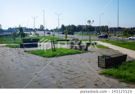 Modern public rest area with wooden benches on paved square next to city highway under blue sky for urban infrastructure Modern public rest area with wooden benches on paved square next to city highway under blue sky for urban infrastructure 143125529