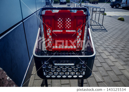 Empty plastic shopping cart with red child seat standing on paved sidewalk near supermarket entrance outdoors for retail business Empty plastic shopping cart with red child seat standing on paved sidewalk near supermarket entrance outdoors for retail business 143125534